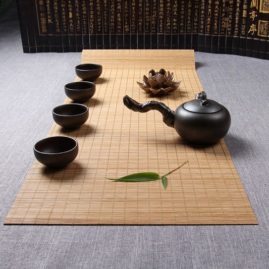 Chemin de table en bambou, couleur beige, une théière et quatre tasses  marron foncé posé dessus.